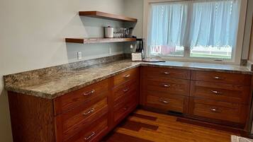 A kitchen with wooden cabinets, granite countertops, and a window with sheer curtains.