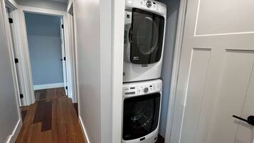 A laundry room with a stacked washer and dryer, wooden flooring, and a door leading to another room.
