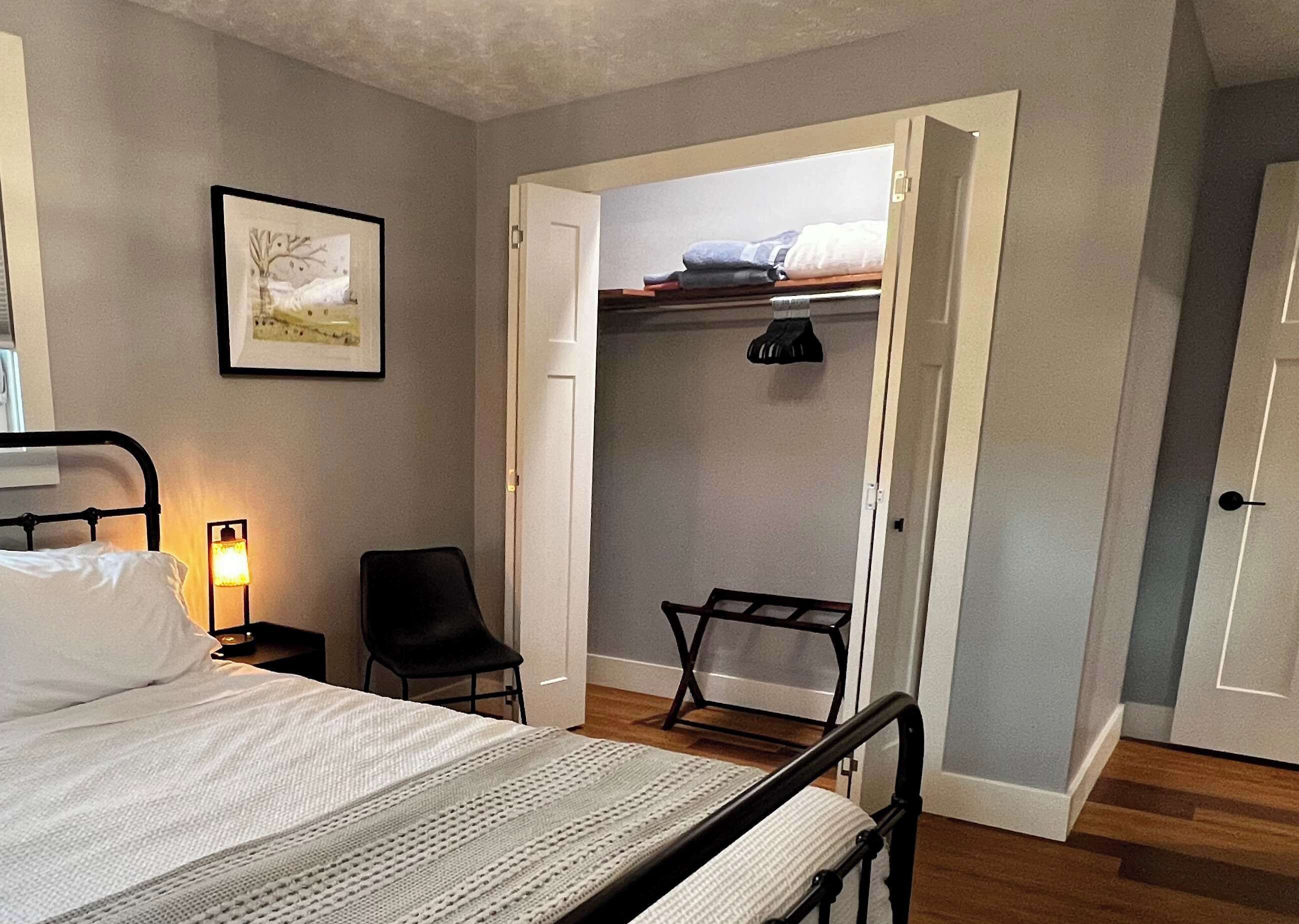 Een slaapkamer met een bed, een stoel, een kledingkast en een ingelijst kunstwerk aan de muur.