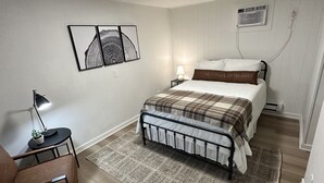 A bedroom with a bed, a nightstand, a lamp, a chair, and a rug. - Rockwell Commons (Rockwell City)