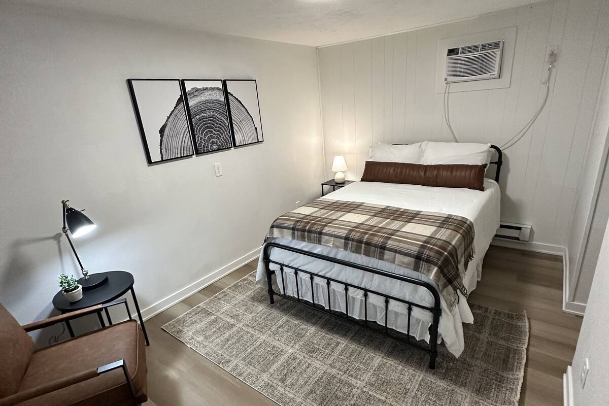 Ein Schlafzimmer mit einem Bett, einem Nachttisch, einer Lampe, einem Sessel und einem Teppich.