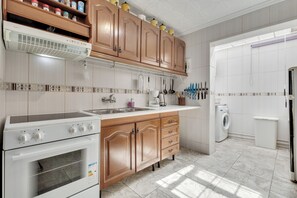 A modern kitchen with wooden cabinets, a built-in oven, a washing machine, and a variety of kitchen utensils. - Hogar del Corazon - Lakefront - Pets Welcome! (Torrevieja)