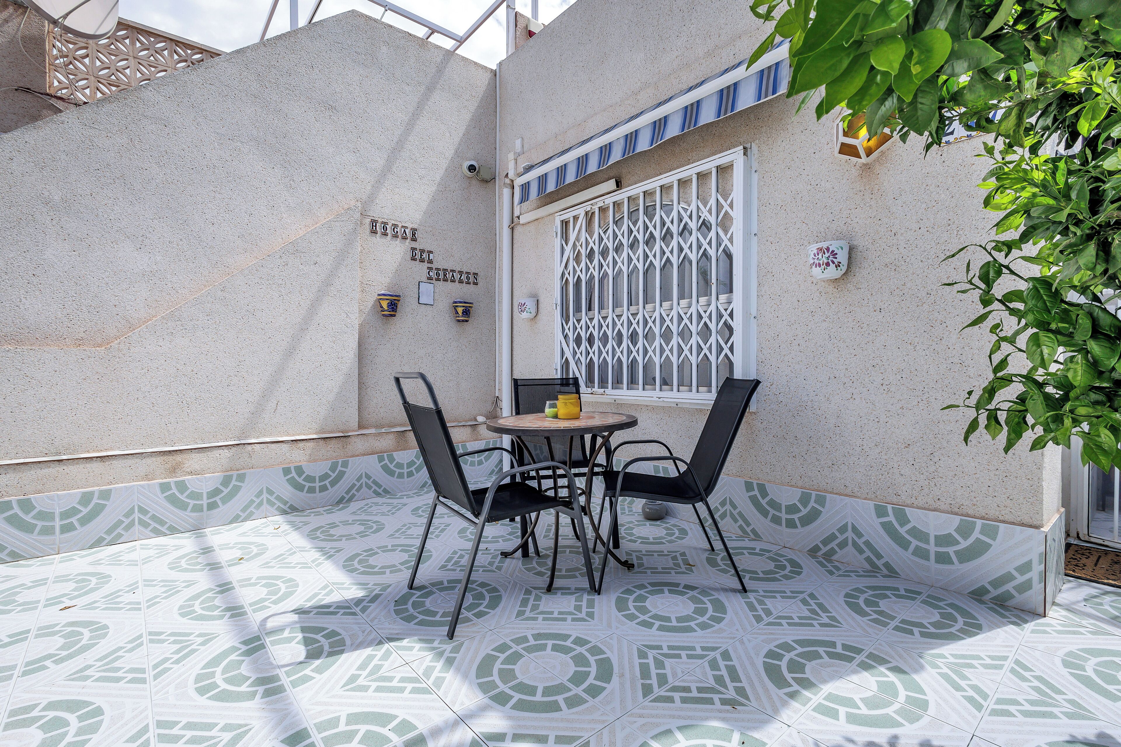 A patio with a table and chairs, a window with a metal grille, and decorative tiles on the walls.