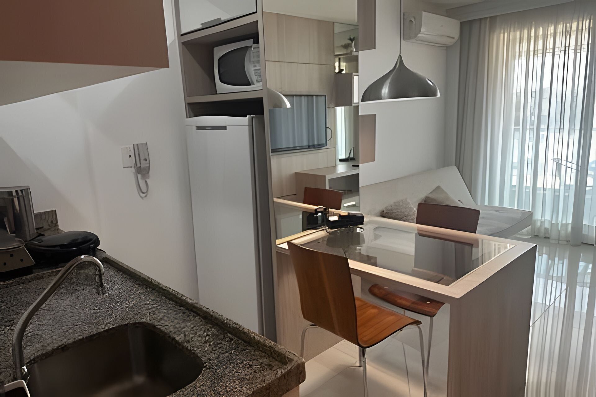 A modern kitchen with a central island, a dining area with a glass table, and a living space with a sofa and a large window.