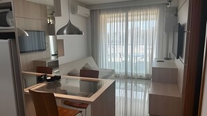 A modern kitchen with a glass dining table, a built-in oven, and a TV mounted on the wall. - Brisas do Lago - apt 13 (Brasília)