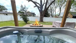 Una vasca idromassaggio con un braciere sullo sfondo, circondata da un patio in legno e un prato.