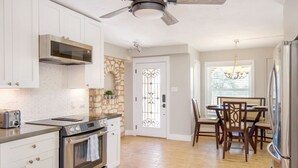 Una cocina con armarios blancos, horno empotrado, microondas y ventilador de techo.