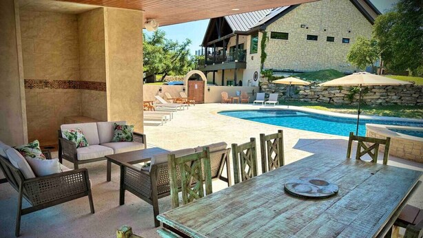 Un patio exterior con piscina, zona de estar y un edificio de piedra al fondo.