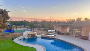 Una piscina con cascada, rodeada por una terraza con mobiliario exterior y vistas a la puesta de sol.