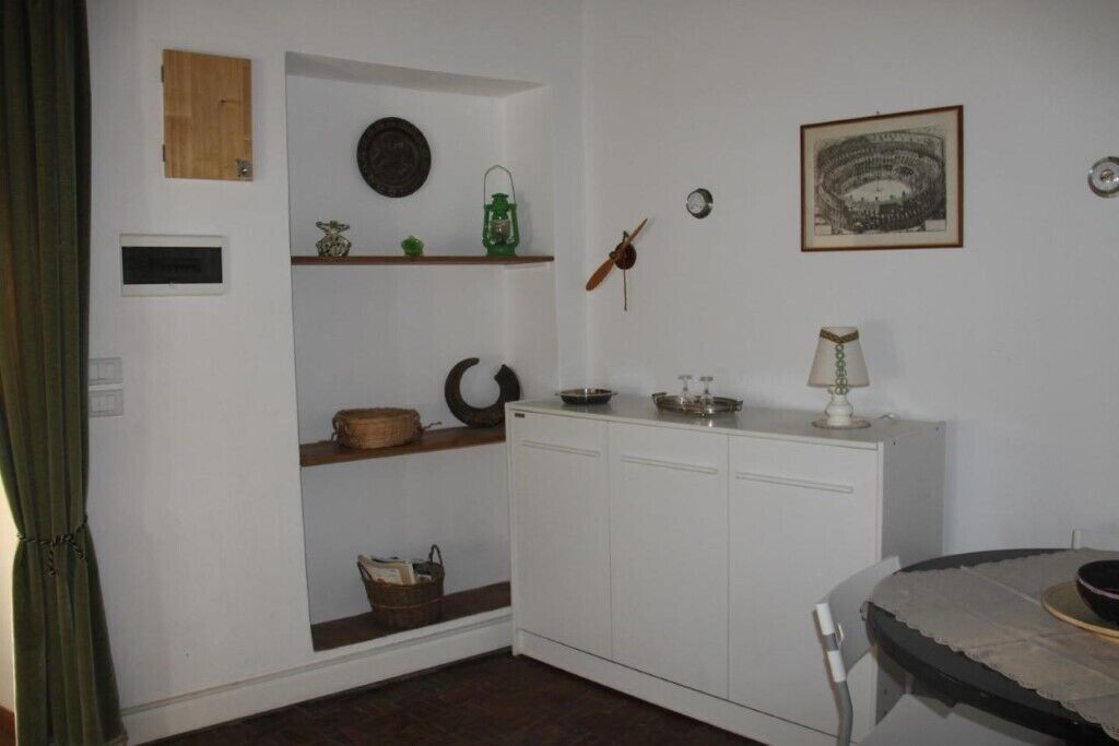 A small, compact room with white walls, a wooden cabinet, a shelf with decorative items, and a framed picture on the wall.