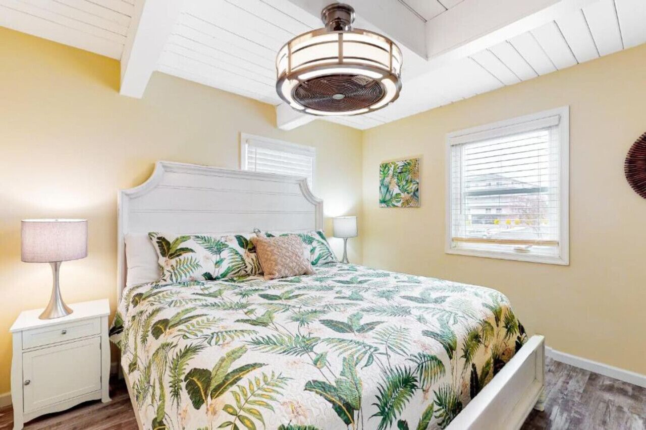 A bedroom with a bed, nightstands, a ceiling fan, and a window with blinds.