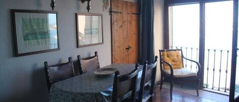 A dining area with a wooden table and chairs, framed pictures on the wall, a wooden door, and a balcony with a railing.