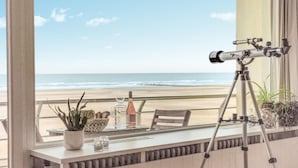 A balcony with a telescope, a table with a bottle, and a view of the beach.