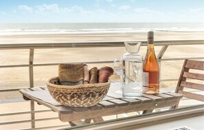 A table with a woven basket, a bottle, and glasses on a balcony overlooking a beach. - Beach front apartment in Oostende (Oostende)