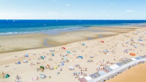 A beach with numerous sunbeds and umbrellas, a sandy shore, and a clear blue sky.