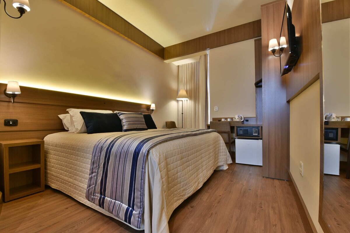Ein Hotelzimmer mit Bett, Nachttischlampen, einem Schreibtisch mit Mikrowelle und einem an der Wand befestigten Fernseher.