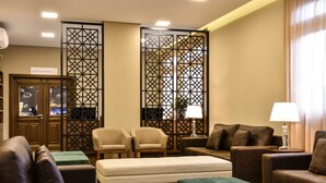 A hotel room with a sofa, armchairs, a small table with a lamp, a decorative screen, and a sign indicating a cafe. - Pousada Stillo Gramado Exclusive (Gramado)