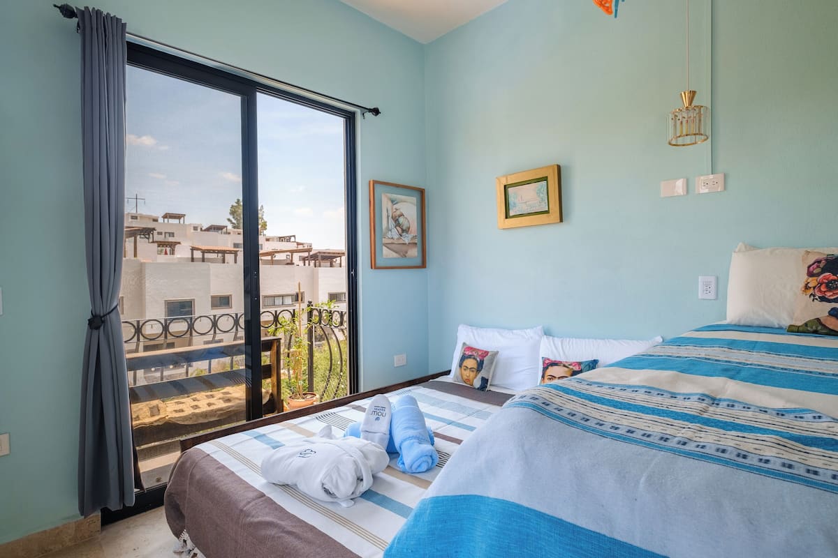 A hotel room with a bed, a window with curtains, a balcony, and a wall with two framed pictures.
