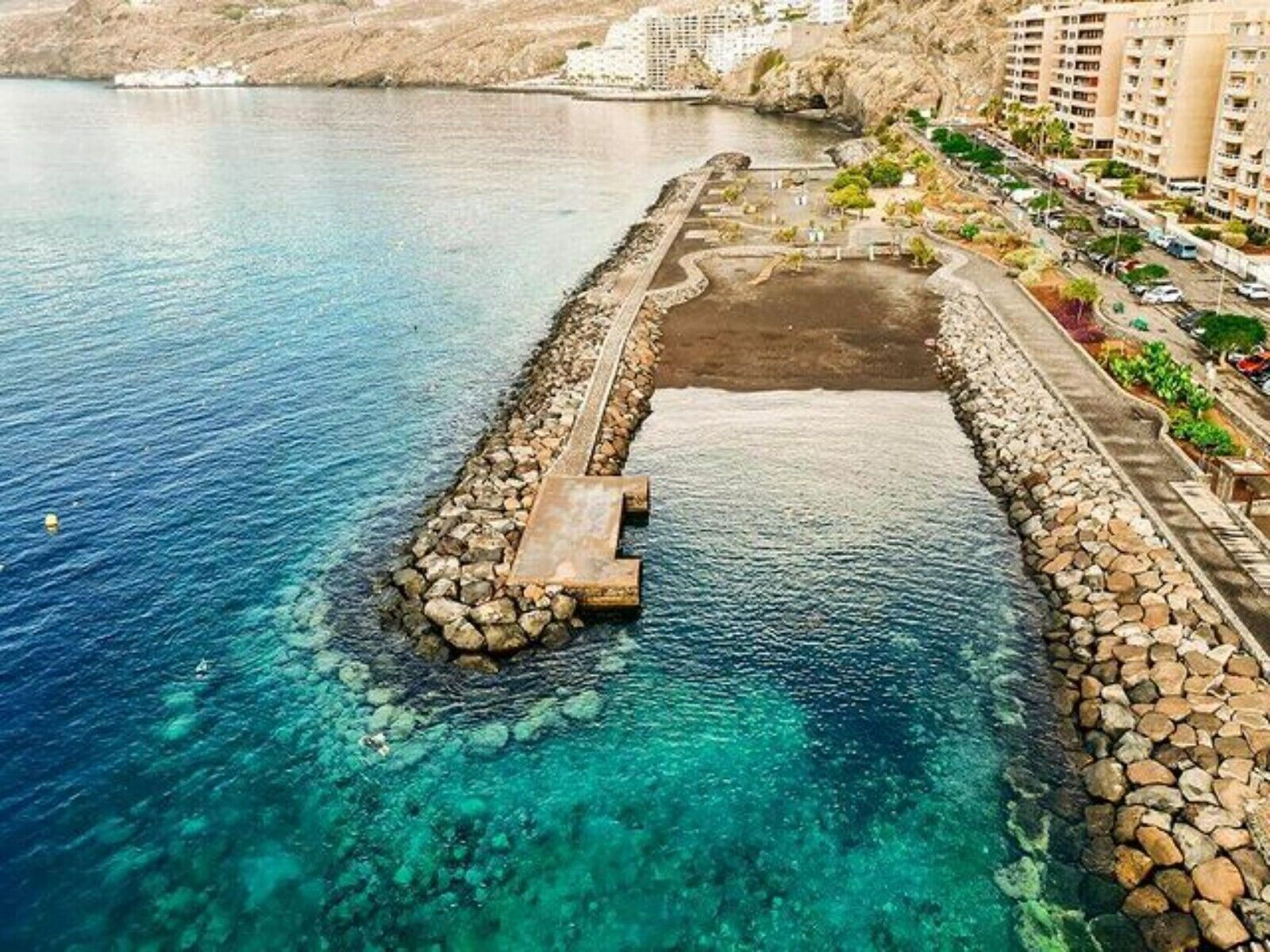 Ein Küstenhotel mit felsiger Uferlinie, klarem blauen Wasser und einem gepflasterten Weg zum Meer.