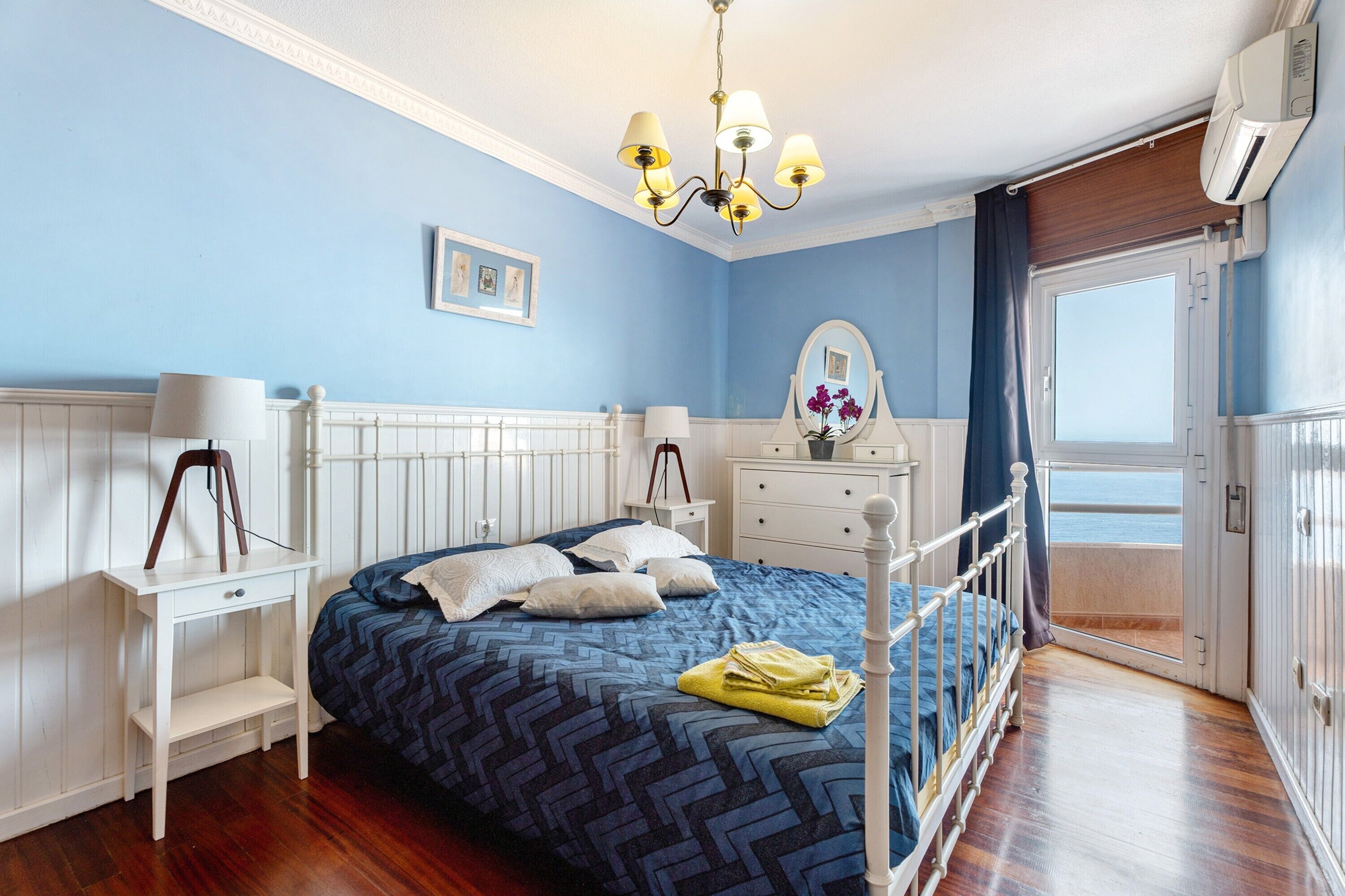 Ein Schlafzimmer mit Bett, Nachttischen, einem Schminktisch und Blick auf das Meer.