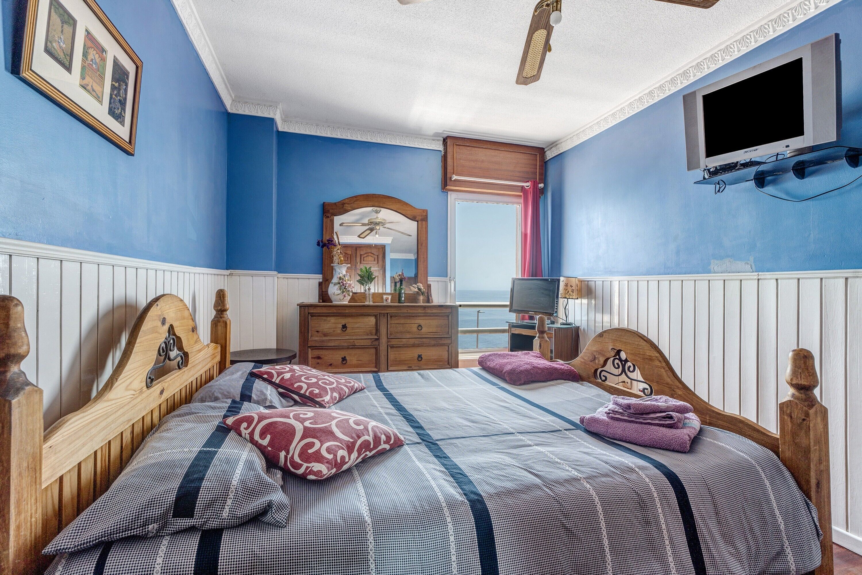 A bedroom with a wooden bed, a dresser, a television, and a window with a view.
