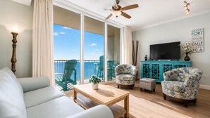 Een woonkamer met een bank, twee fauteuils, een salontafel, een televisie en een balkon met stoelen.