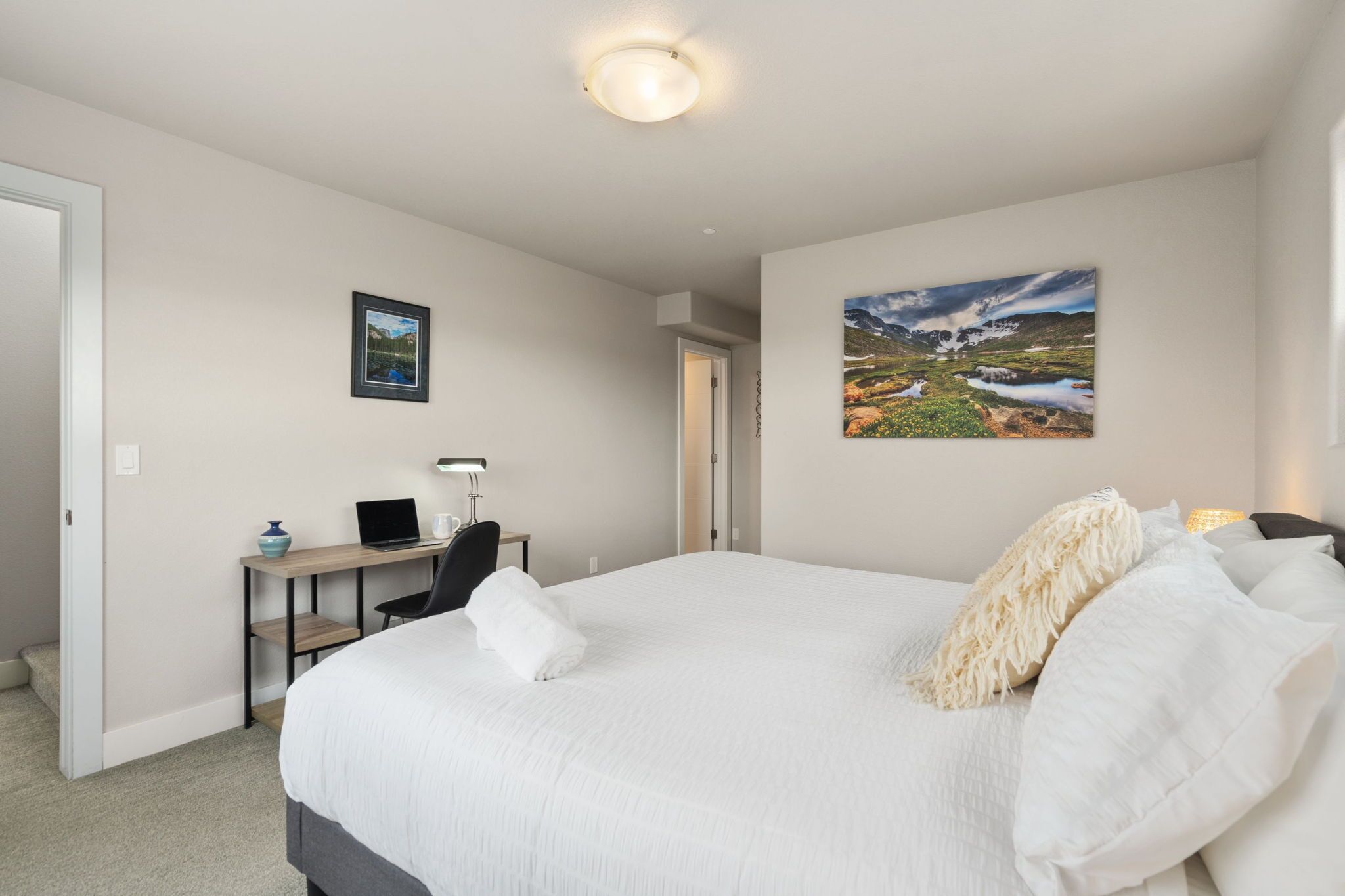 A hotel room with a large bed, a desk with a laptop, a chair, and two framed pictures on the walls.