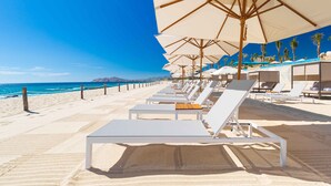 A beachside hotel with sun loungers and umbrellas, a clear blue sky, and the ocean in the background. - Luxury 2 Bedroom Suite with wonderful "lazy river" in Los Cabos (San José del Cabo)