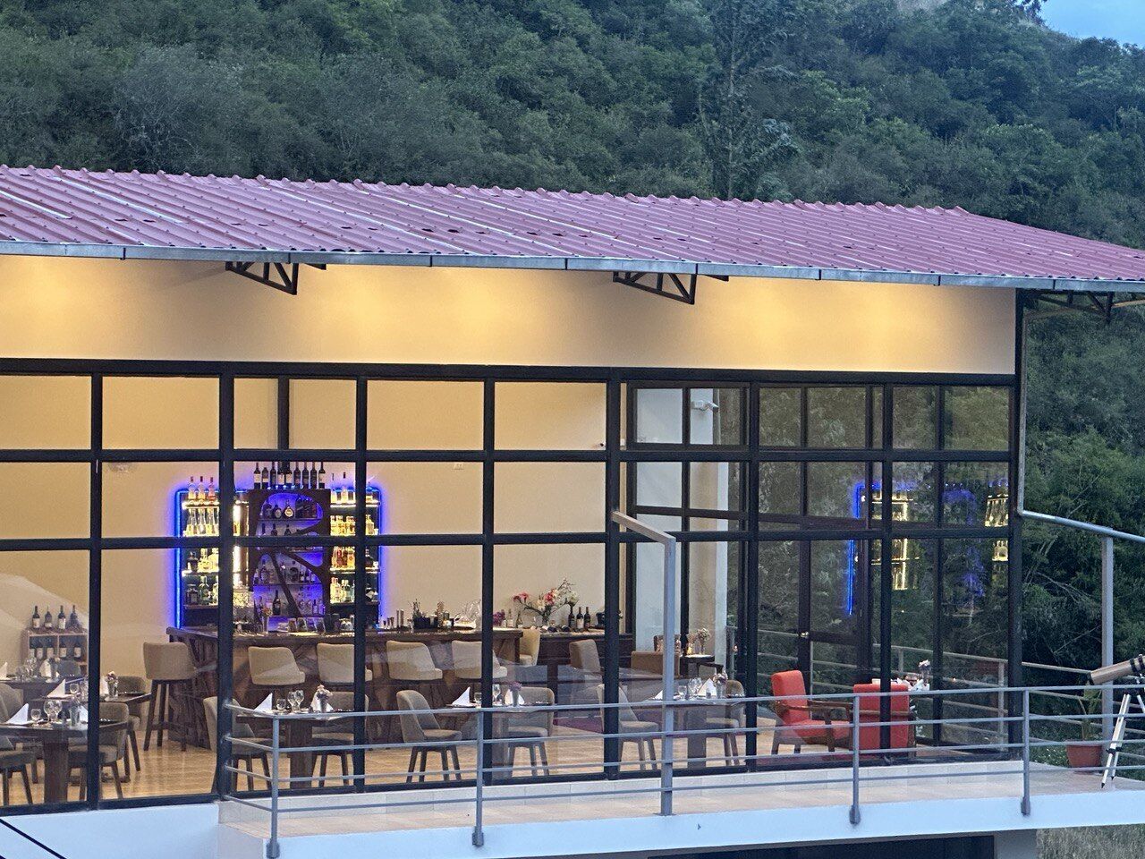Um restaurante com um espaço envidraçado, mesas ao ar livre e um bar com prateleiras iluminadas.