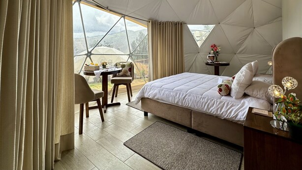 A spacious tented room with a bed, a table with chairs, and a view of mountains. - Miski Samay Domo Boutique (Urubamba)