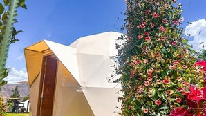A tent-like structure with a clear entrance, surrounded by lush greenery and flowers. - Miski Samay Domo Boutique (Urubamba)