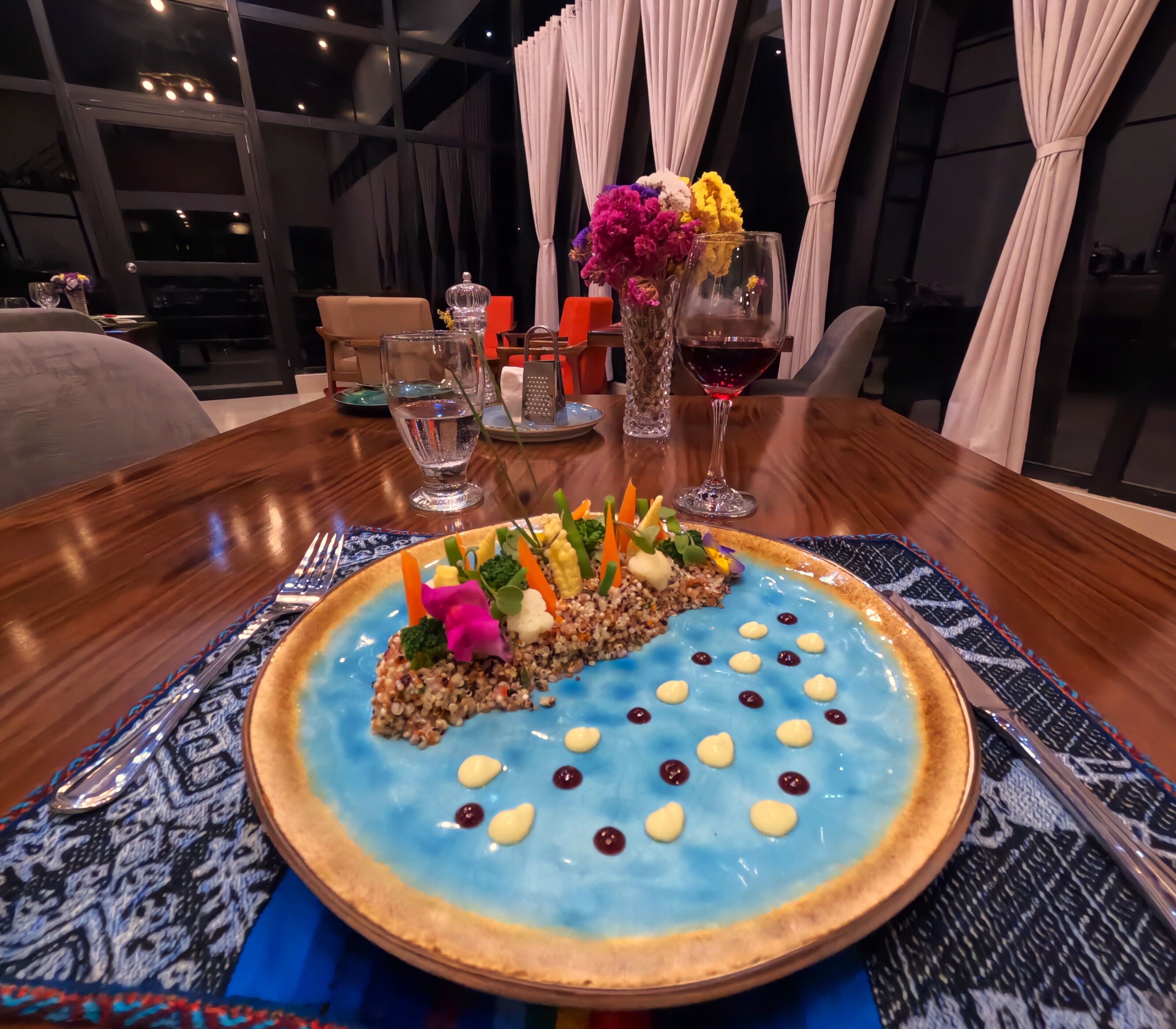 A dining table with a blue dessert, a glass of water, and a glass of red wine.
