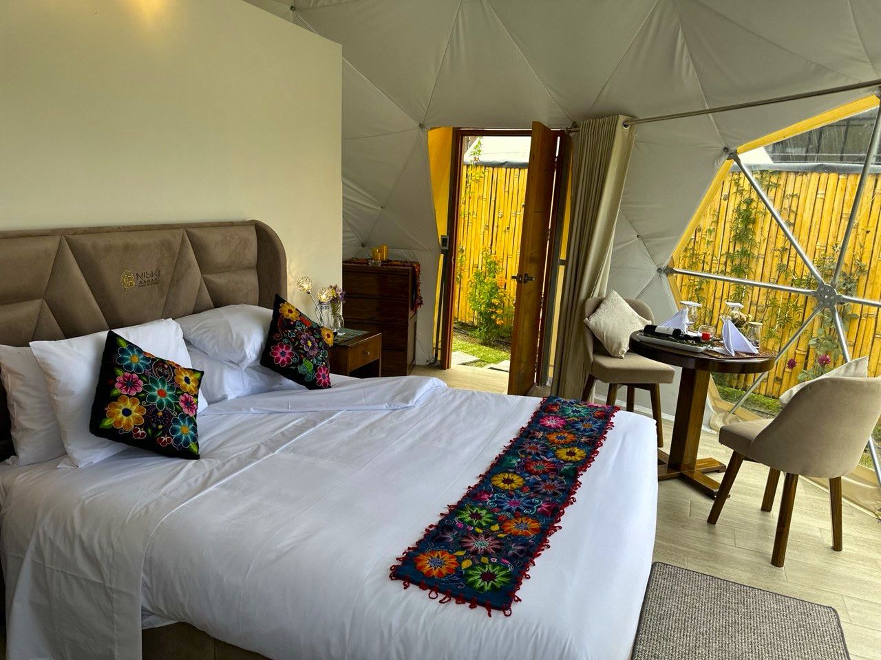 A tented accommodation with a bed, pillows, a table, and chairs.