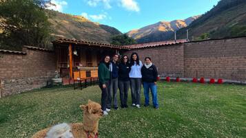 Un gruppo di persone in piedi in una zona erbosa, con un edificio sullo sfondo e montagne all'orizzonte.