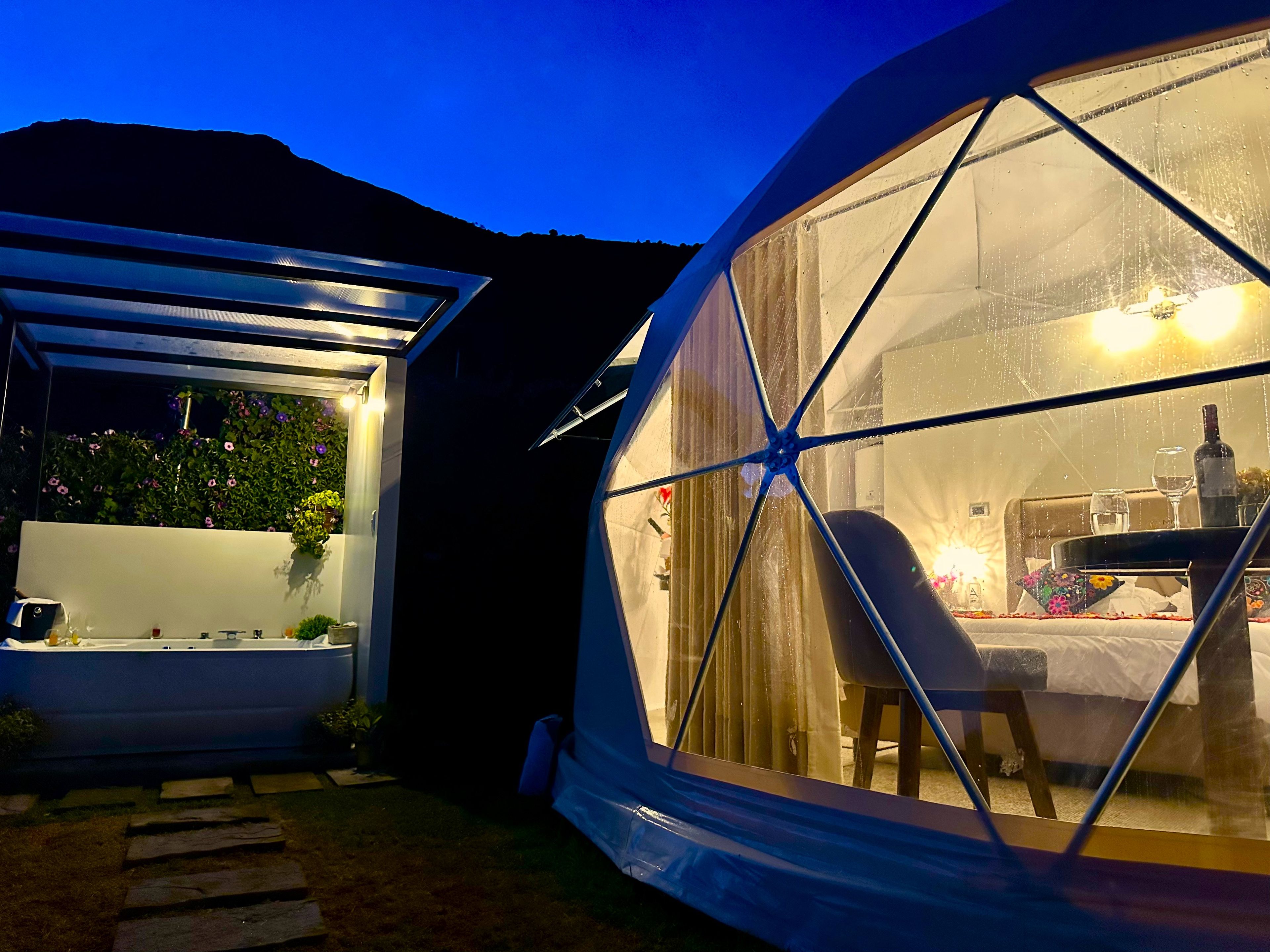 A geodesic dome structure with a dining area inside, featuring a table and chairs, and a view of the surrounding landscape.