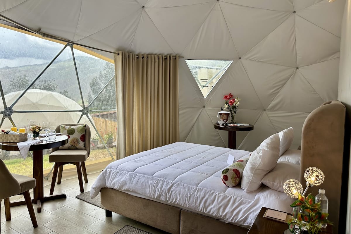 A tented room with a bed, a table, chairs, and a small table with a vase of flowers.