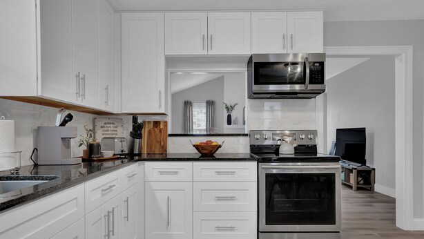 A modern kitchen with white cabinetry, stainless steel appliances, and a black countertop.