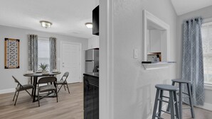 A modern kitchen with a built-in refrigerator, a dining area with a round table and chairs, and a bar area with stools.