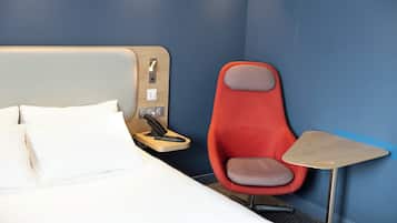 Une chambre d’hôtel avec un lit, une chaise rouge, une petite table et un téléphone sur une table de chevet.