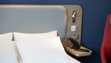 Habitación de hotel con cama, almohadas, mesita de noche con teléfono y toma de corriente.
