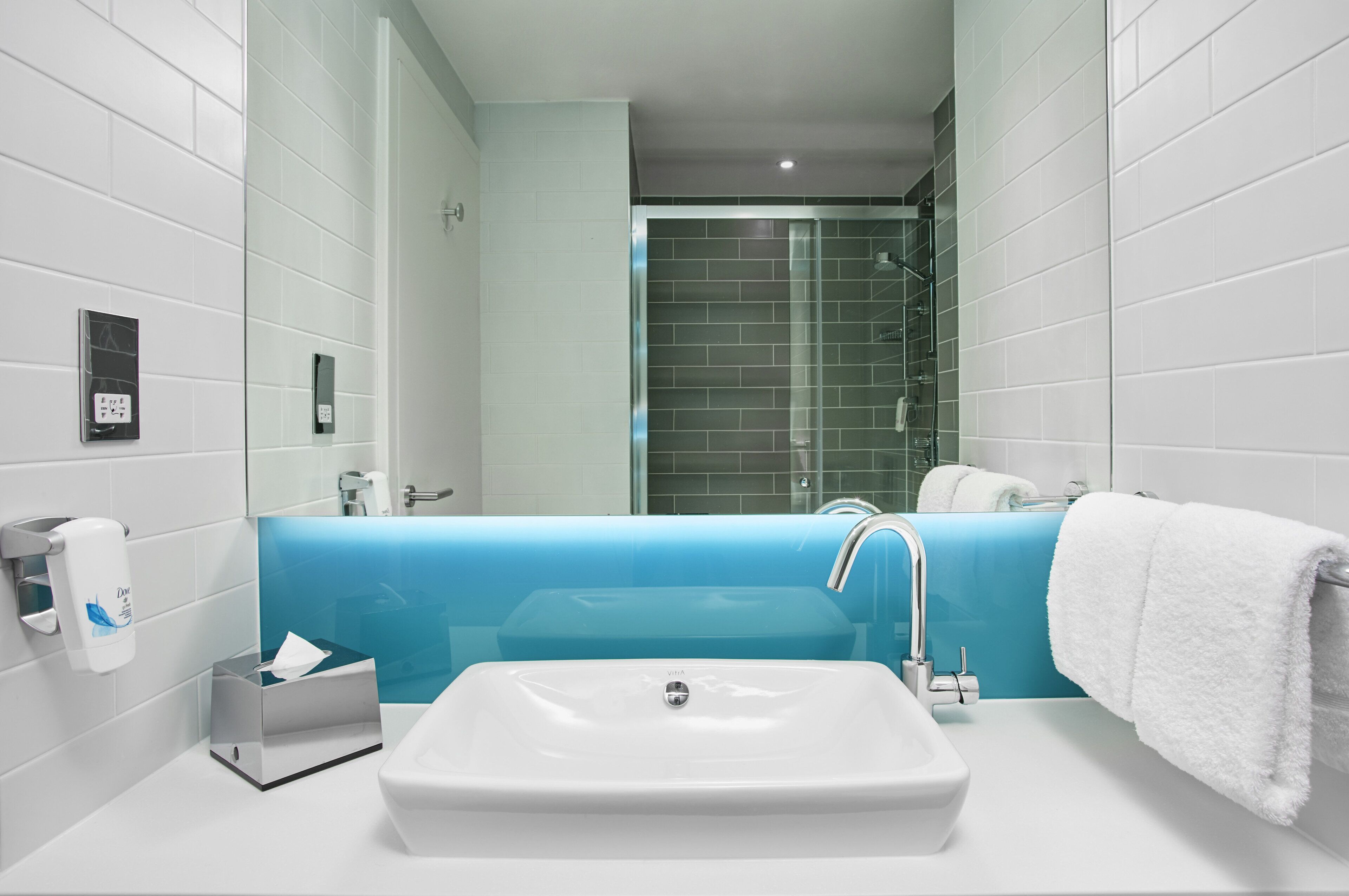 Une salle de bain moderne avec un lavabo blanc, un mur d’accent bleu et une cabine de douche en verre.