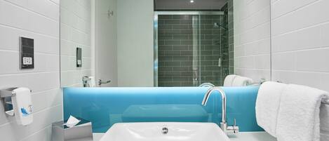 A modern bathroom with a white sink, a blue accent wall, and a glass shower enclosure.