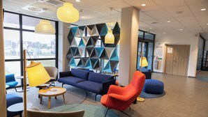 A modern lobby with a blue sofa, orange armchair, and round tables. - Holiday Inn Express Caen Epron by IHG (Epron)