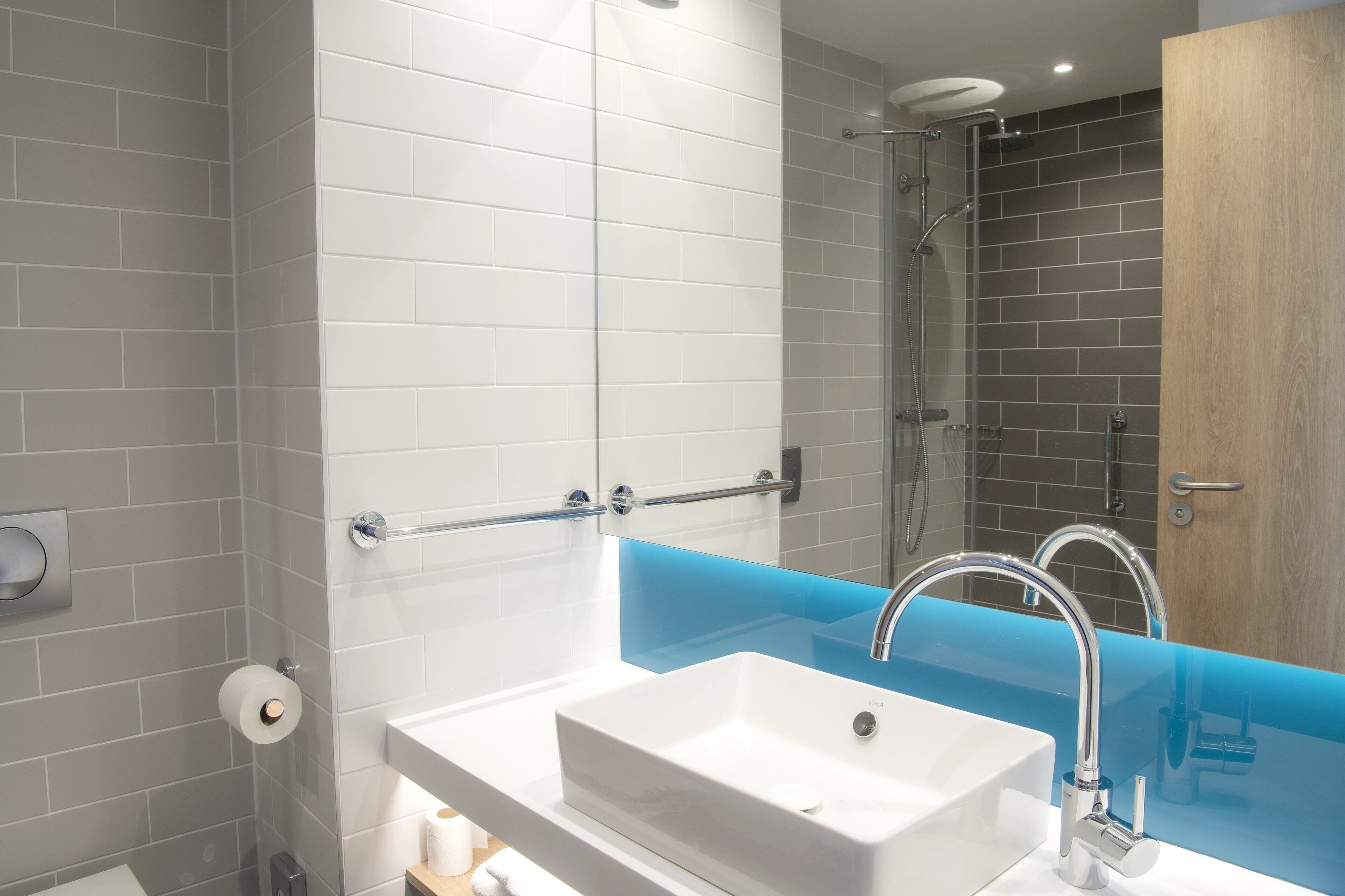 A modern bathroom with a white sink, a glass shower enclosure, and a wooden door.
