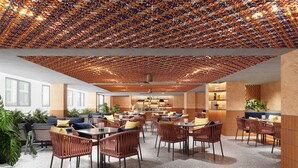 A modern restaurant with a unique ceiling design, featuring a pattern of small, colorful objects. The space includes several dining tables and chairs, with a mix of wicker and metal furniture. There are potted plants and a variety of seating options, including sofas and high tables. The walls are adorned with textured panels and shelves displaying decorative items. - voco Bali Seminyak by IHG (Keroboken Kelod)