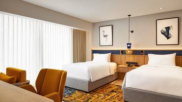 A hotel room with two beds, a wooden desk, a chair, and a patterned rug.
