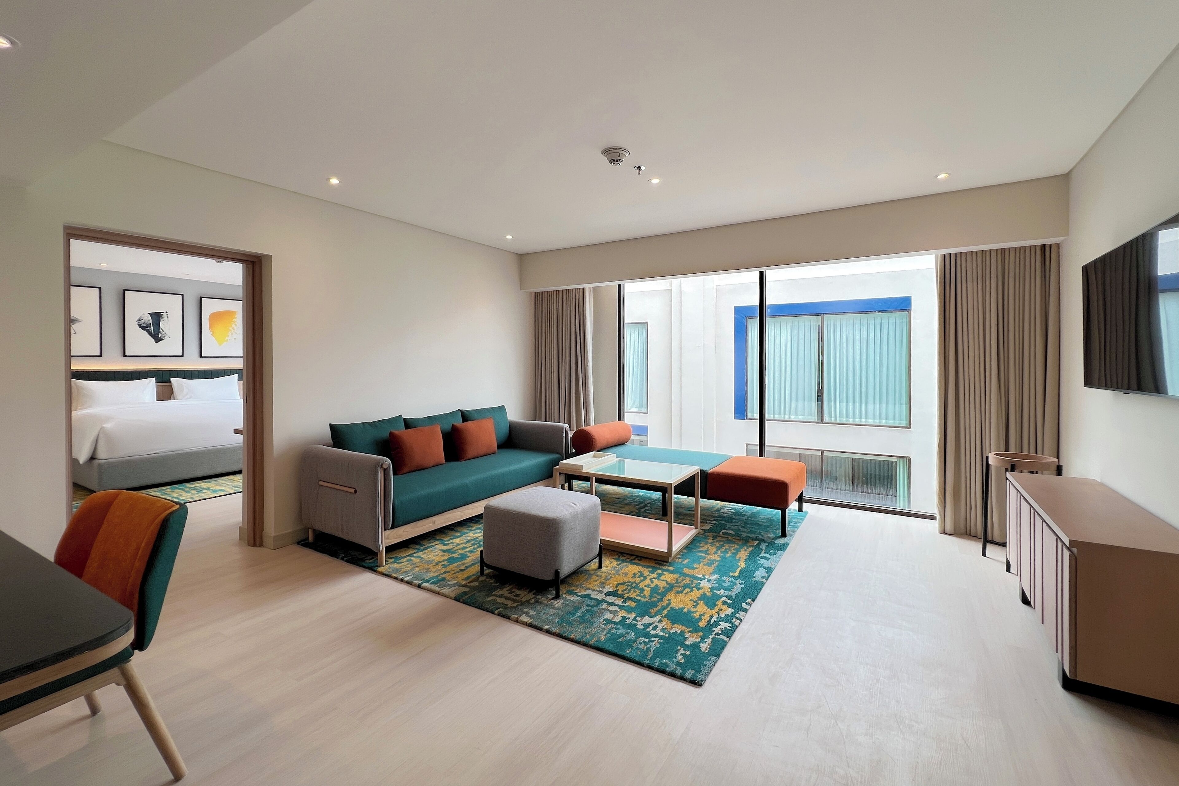 Una habitación de hotel moderna con cama, sofá, reposapiés, mesa de centro y televisión.