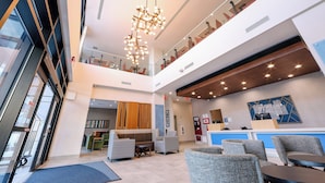 Un moderno vestíbulo de hotel con recepción, zona de estar y una escalera que sube a un nivel superior.
