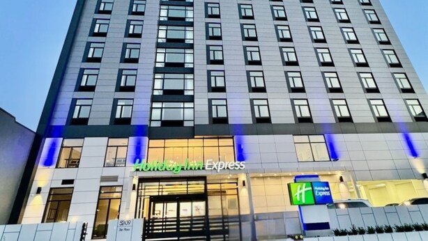 A high-rise hotel with a modern design, featuring a prominent 'Holiday Inn Express' sign at the ground level. - Holiday Inn Express Long Island City E New York by IHG (Long Island City)