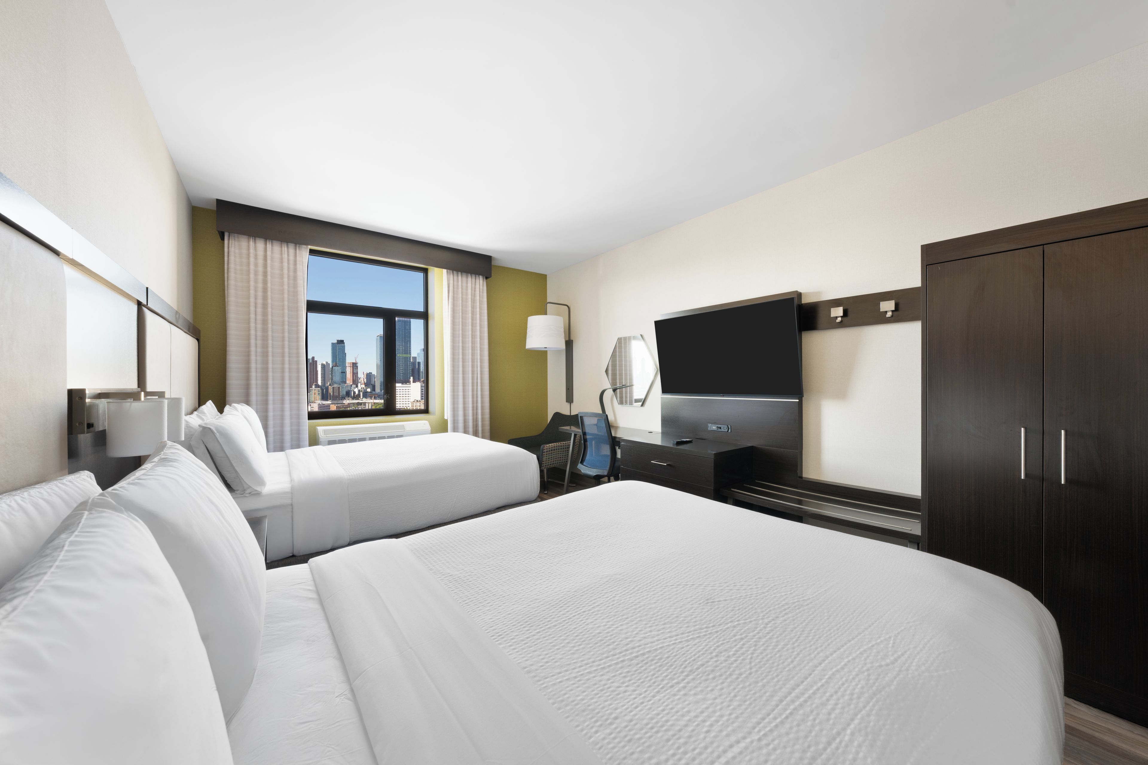 A hotel room with two beds, a television, and a city view.